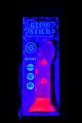 Glow Stick silicone dildo with heart motifs shown under UV light, curved shaft and suction base inside display packaging.