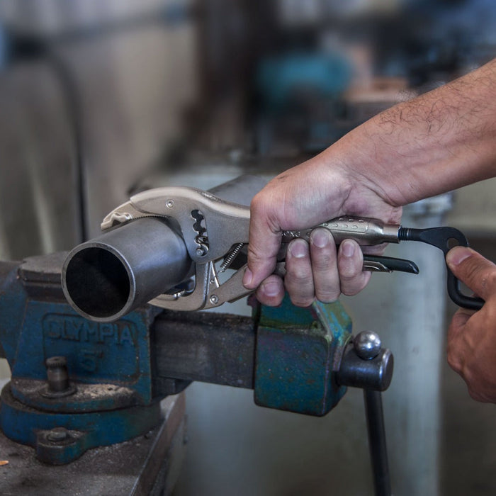 StrongHand PAJ100 pliers gripping a pipe while the crank handle is adjusted; workpiece and vice shown for demonstration.
