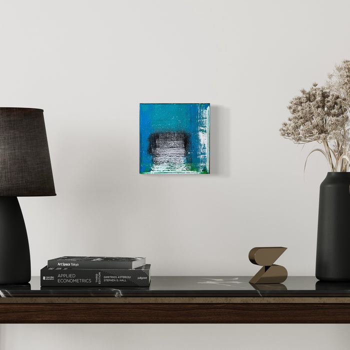 The artwork 'Voyage 2' by Bill Burns features a small square canvas with vibrant turquoise blue borders framing a textured grayscale center. The abstract composition creates a portal-like effect through layered acrylic paint, with rough brushstrokes and distressed textures merging modern and industrial aesthetics in an 8x8 inch format. Artwork by Bill Burns.